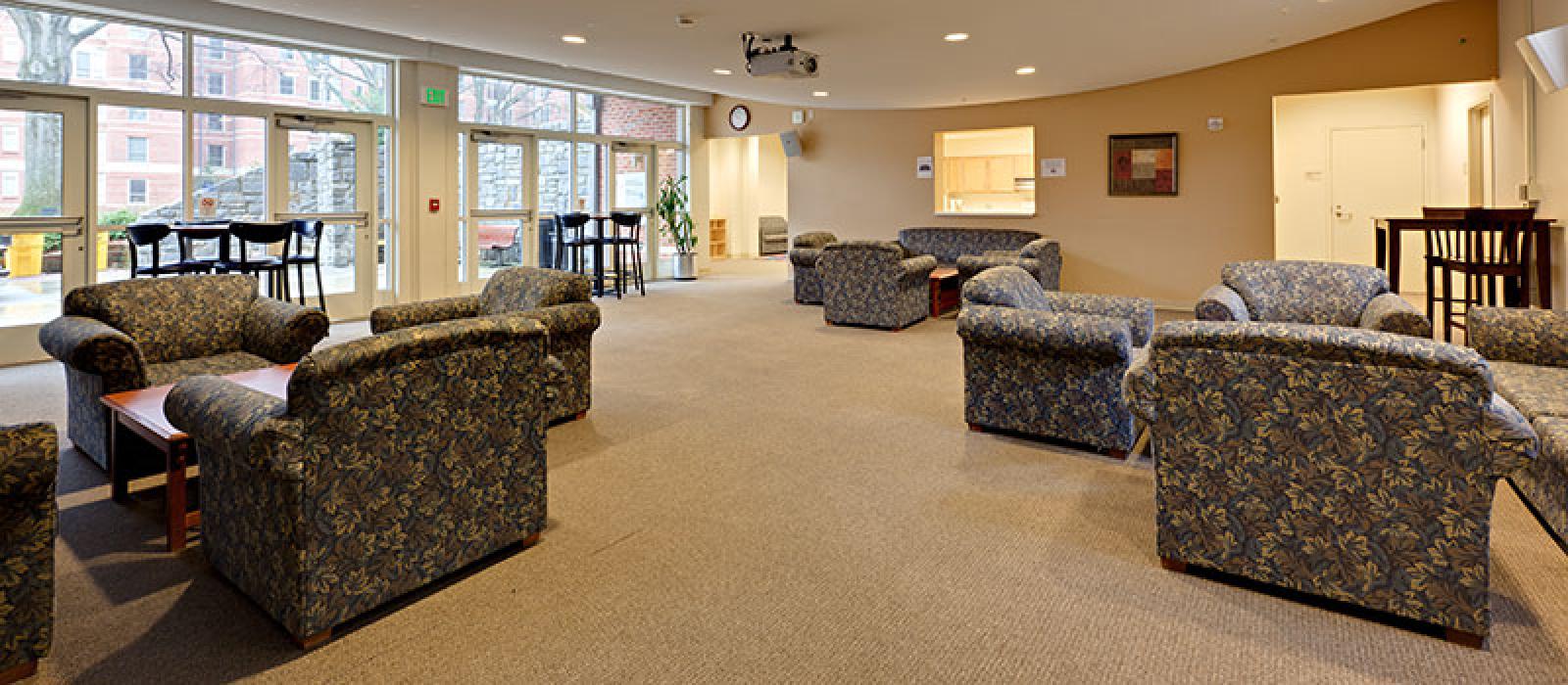 Activity room. Sofas, bar tables with bar stools, and a kitchen in the background.