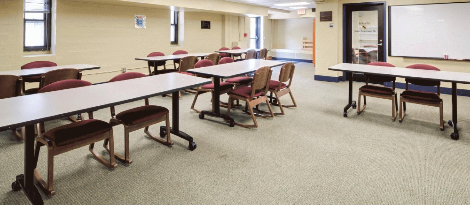 Activity room with a screen, long tables and chairs.