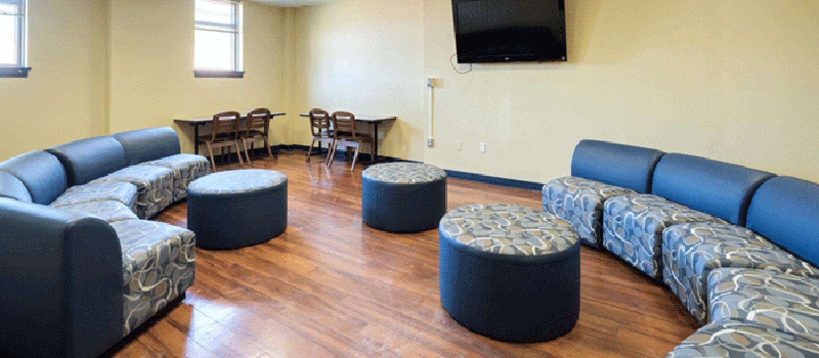 Living area with chairs placed together as a sofa, three table, a TV and tables against the wall with table chairs.