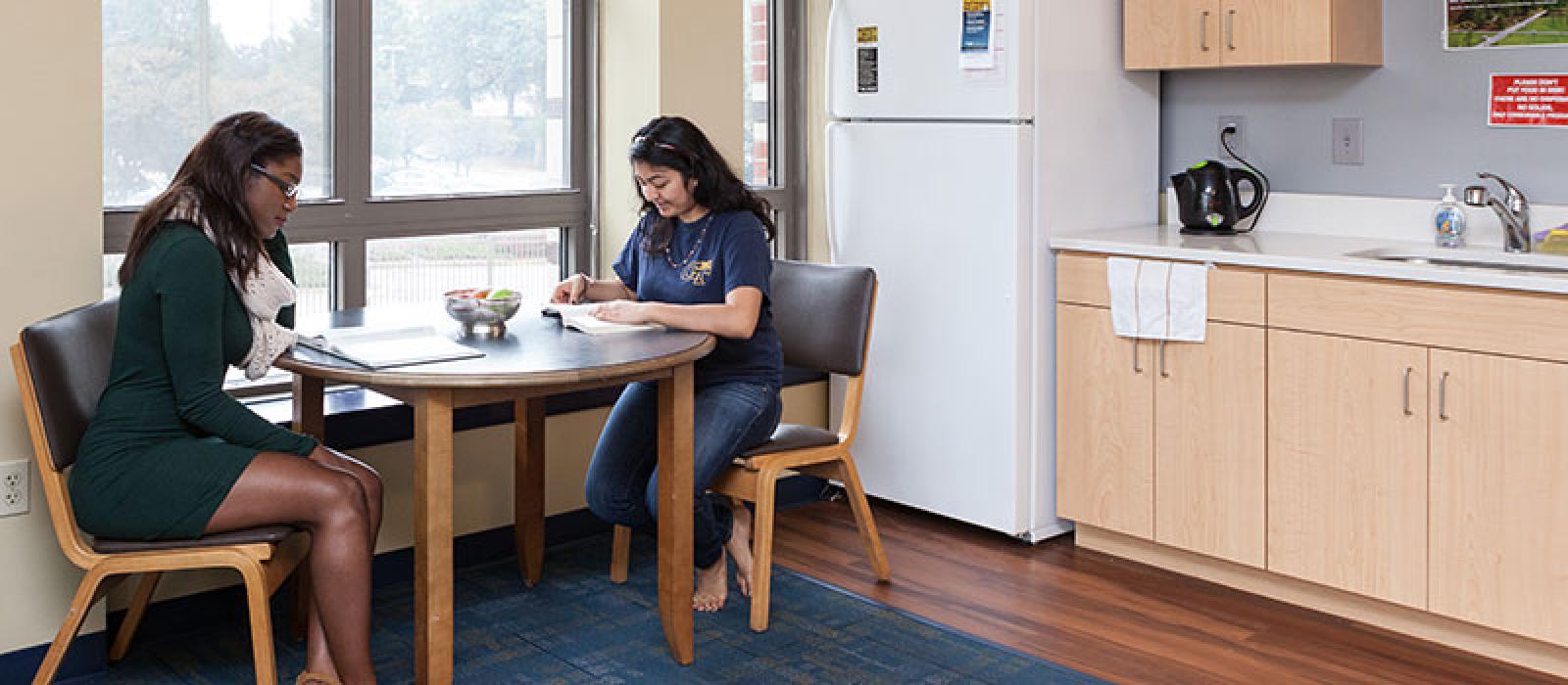 Two young women reading at a dining table in a kitchen.