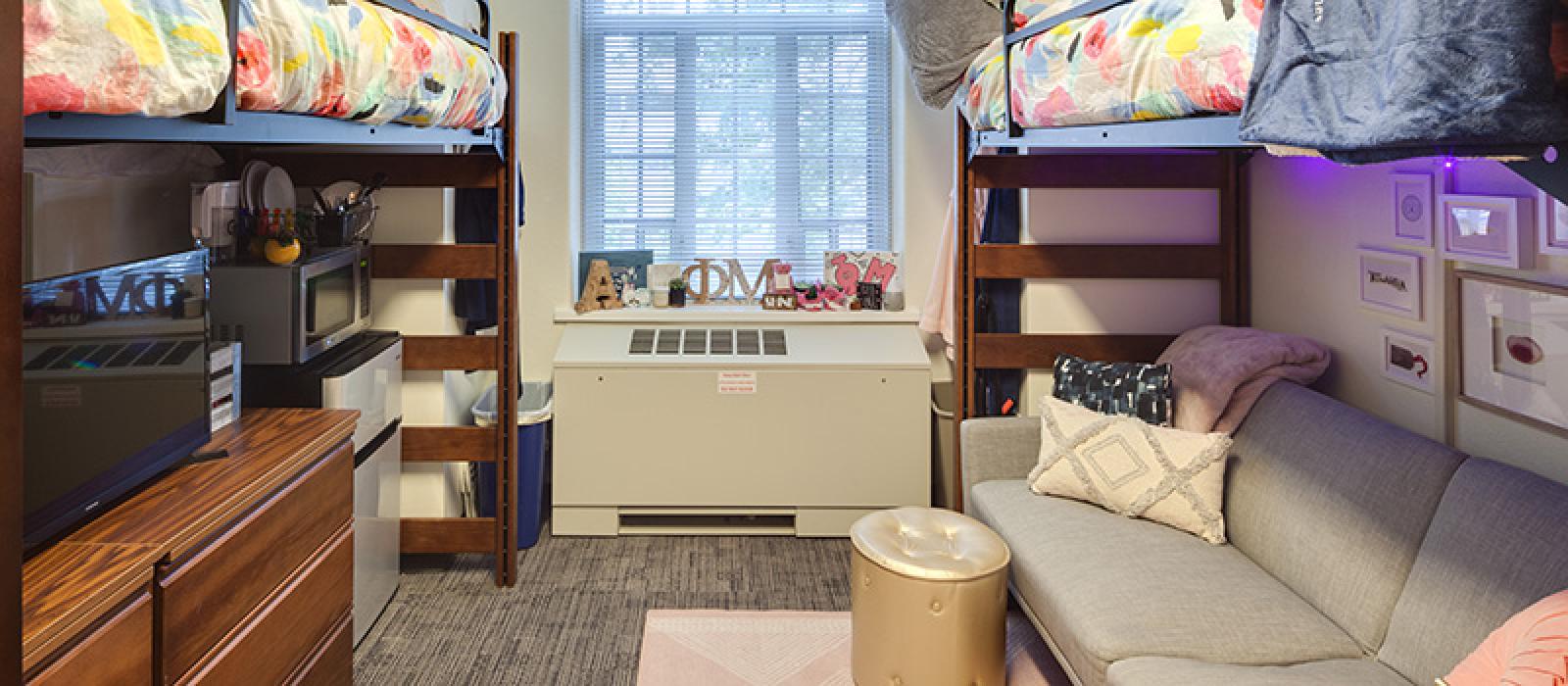 Two bunk beds. One with a small fridge and a dresser underneath another one with a small sofa.