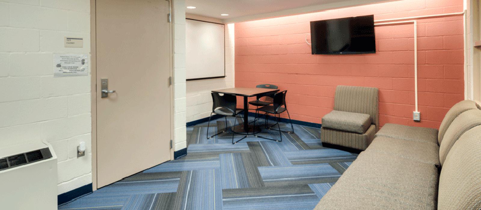 Study room with a sofa sectional, table, chairs and a TV monitor on one of the walls.