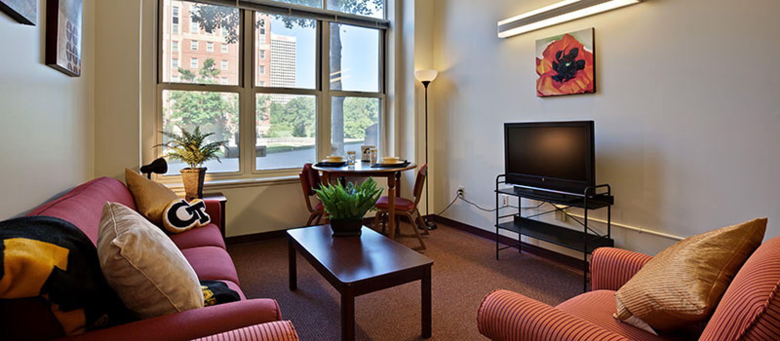 Living room furnished with a sofa, arm char, coffee table, TV and a table with two chairs.