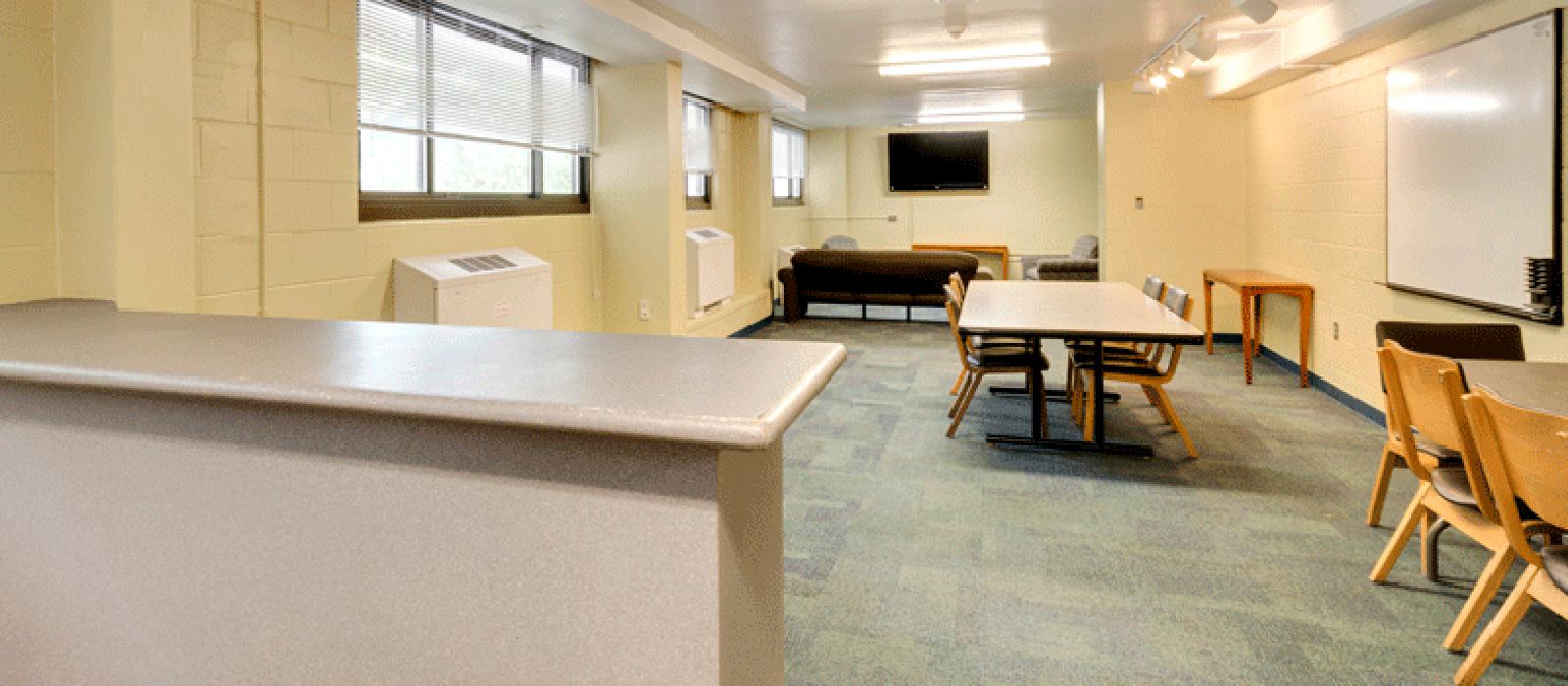 Lounge area furnished with tables and chairs, sofa, a counter, and a white board.