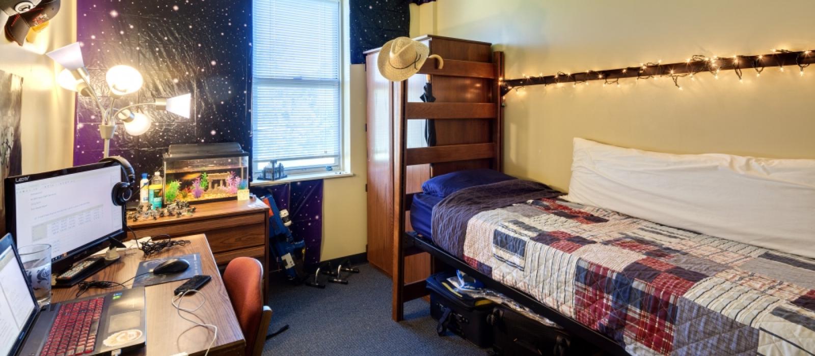 Furnished bedroom with a bed, desk and wardrobe decorated by a student.